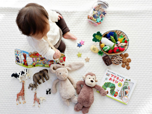 En liten flicka sitter på golvet omgiven av leksaker.