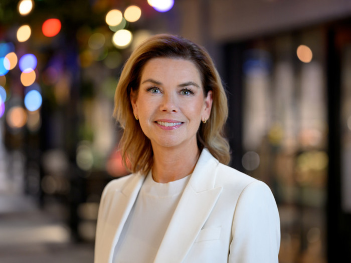 En kvinna i vit kostym står framför en byggnad.